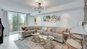 Una sala de estar moderna con un sofá grande, dos mesas de centro y una zona de comedor con sillas.