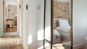Een slaapkamer met een stenen muur, een bed met witte lakens, een houten vloer en een spiegel die de kamer weerspiegelt.