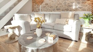 Een woonkamer met een stenen muur, een grijze bank, een ronde salontafel en een trap.