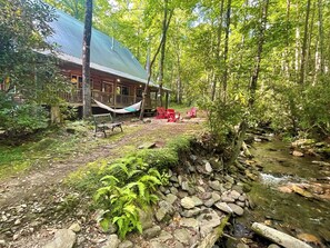 A cabin with a porch, a hammock, and red chairs.