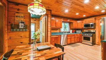 A wooden cabin interior with a dining table, a chandelier, wooden cabinets, a refrigerator, and a stove.