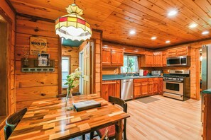A wooden cabin interior with a dining table, a chandelier, wooden cabinets, a refrigerator, and a stove.