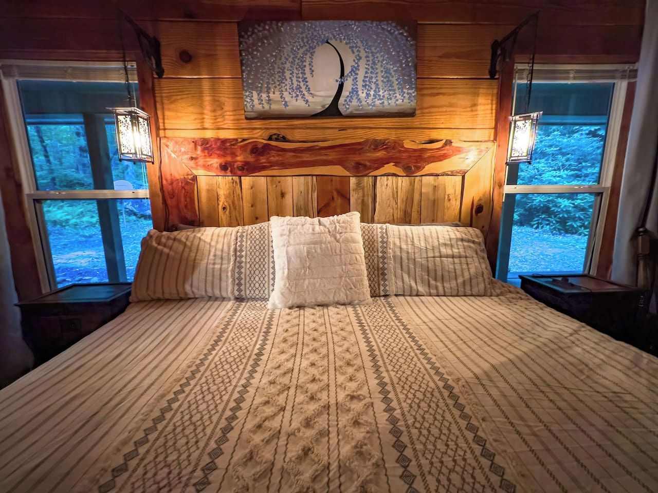 A bed with a patterned bedspread, two bedside lamps, and a wooden headboard with a decorative piece above.