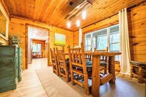 A wooden interior with a dining area featuring a table and chairs, a large window, and a view of the outdoors. - Creekside log cabin near Lake Chatuge & Blue Ridge (Hayesville)
