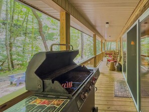 An outdoor covered patio with a barbecue grill, wooden deck, and seating area. - Creekside log cabin near Lake Chatuge & Blue Ridge (Hayesville)