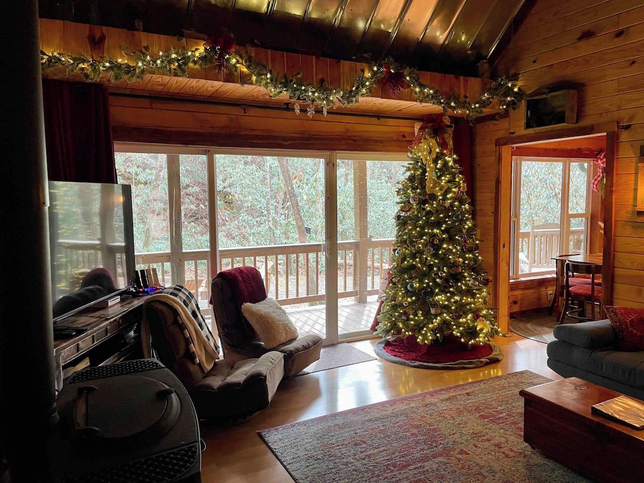 Interior acogedor de una cabaña con un árbol de Navidad, un piano y un ventanal con vistas a una terraza.