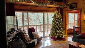 Interior acogedor de una cabaña con un árbol de Navidad, un piano y un ventanal con vistas a una terraza.
