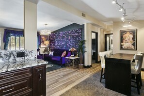 A modern living room with a marble kitchen island, a purple sofa, and a dining area with a black table and white chairs.
