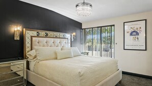 Quarto com uma cama grande, uma mesinha de cabeceira, um candelabro e um pôster na parede.