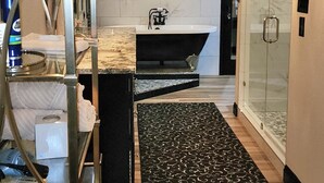Quarto de hotel com banheiro, tapete preto estampado e uma estante de metal.