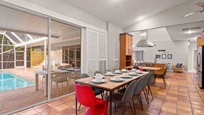 A modern kitchen with a dining area, a pool, and a sliding glass door leading to an outdoor seating area. - Next to IMG Golf! Heated Pool, Spa, Game Room! (Bradenton)