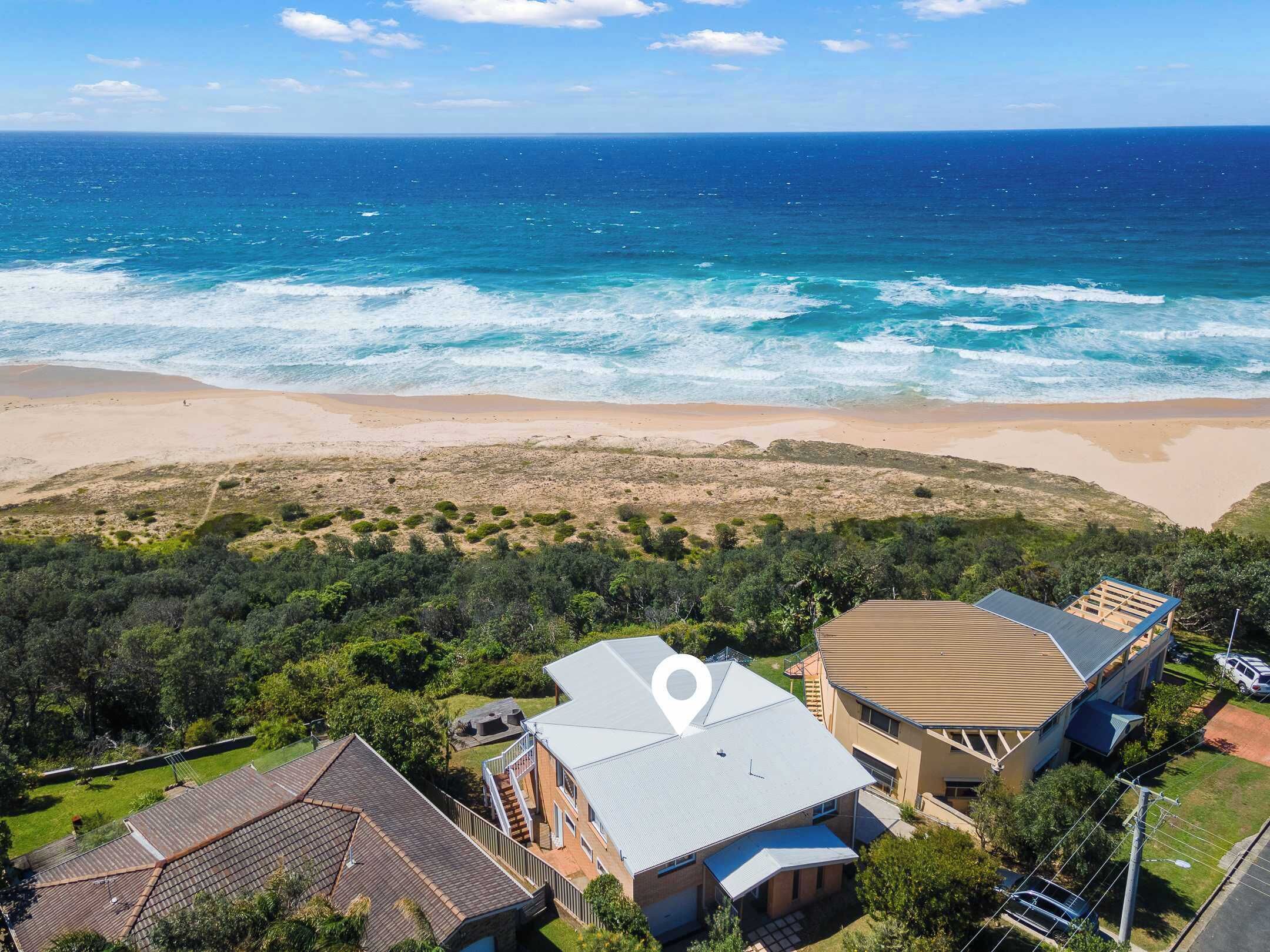 A coastal property with a beach view, a large house with a curved roof, and a smaller building with a flat roof.