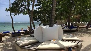 Eine Strandliege mit einer Sitzgruppe in Kreisform, ausgestattet mit einem großen weißen Kissen und einem kleinen Tisch mit einer Flasche und einer Tasse.