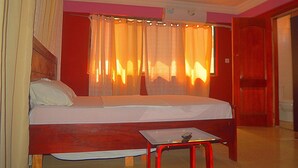 A single bed with a wooden headboard, a small table with a remote control, and a ceiling fan. - Hansonic Hotel (Accra)