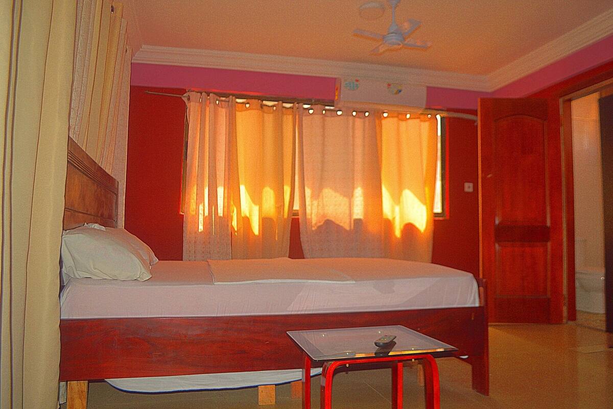 A single bed with a wooden headboard, a small table with a remote control, and a ceiling fan.