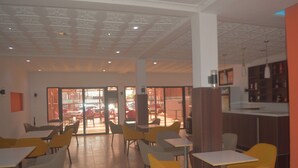 A spacious indoor area with multiple tables and chairs, a bar area, and a view through large glass doors to an outdoor space. - Hansonic Hotel (Accra)