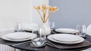 Ein runder Esstisch mit weißen Tellern und klaren Gläsern, gedeckt mit schwarzen Platzsets und Besteck.