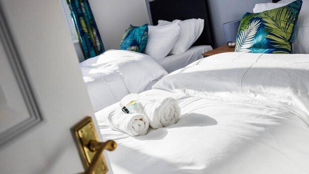 Ein Hotelzimmer mit einem ordentlich bezogenen Bett, weißen Leinentüchern und zwei aufgerollten Handtüchern auf dem Bett.