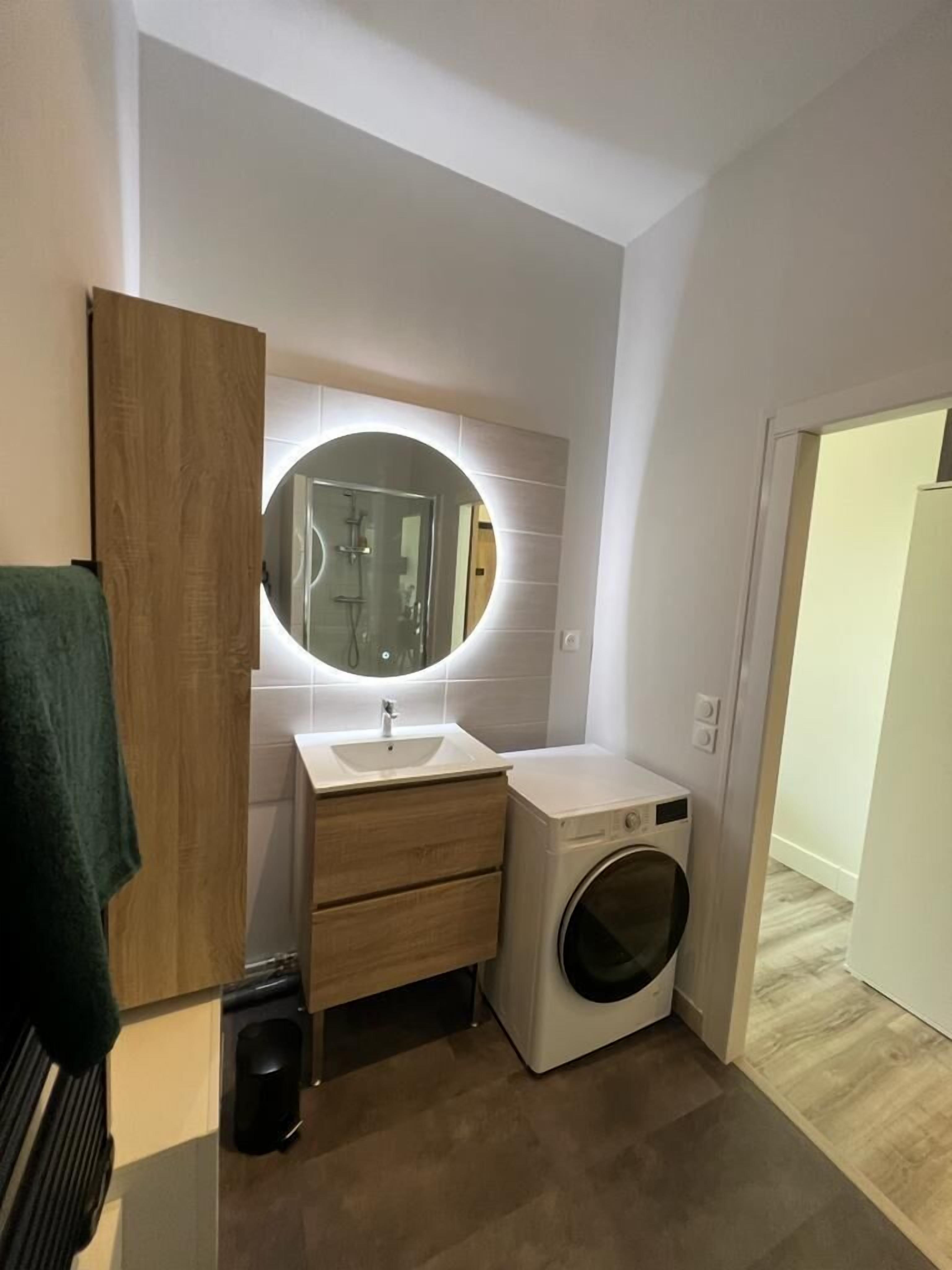 Un baño moderno con tocador de madera, espejo redondo, lavadora empotrada y barra para toallas.
