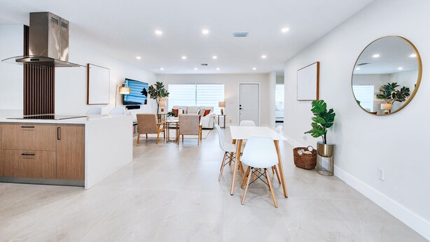 A modern kitchen with a built-in stove, a dining area with a white table and chairs, and a large mirror on the wall.