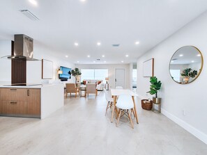 A modern kitchen with a built-in stove, a dining area with a white table and chairs, and a large mirror on the wall. - Lux Family Oasis with Heated Private Pool, King Bed & HD TVs (Dania Beach)
