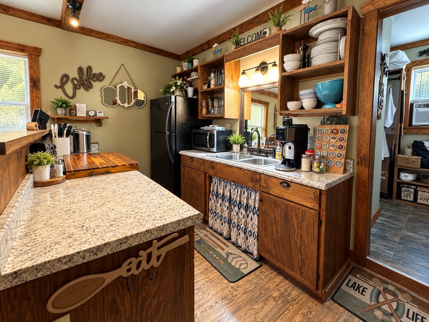 A kitchen with a granite countertop, wooden cabinets, a refrigerator, a microwave, and a coffee station.
