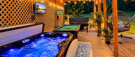 A wooden deck with a hot tub, pool table, and outdoor seating area.