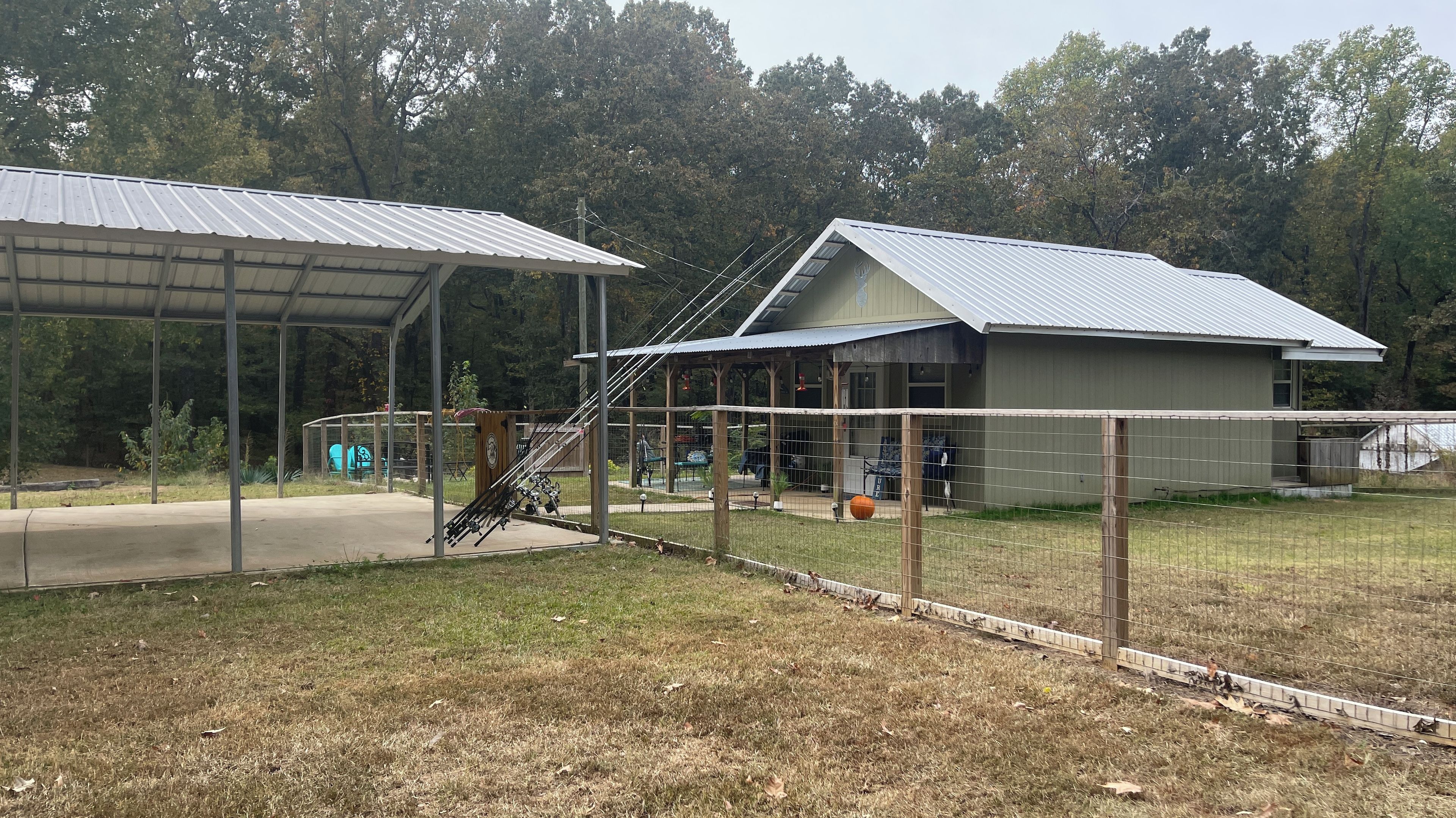 A fenced outdoor area with a covered pavilion and a building with a metal roof.