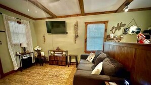 Una sala de estar acogedora con un sofá de cuero marrón, una barra para café y un televisor montado en la pared.
