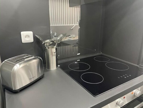 A kitchenette with a stainless steel toaster, a stainless steel container with utensils, and a black induction cooktop with four burners.