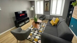 Una sala de estar moderna con un sofá gris, una mesa de centro y un televisor que muestra 'NETFLIX'.