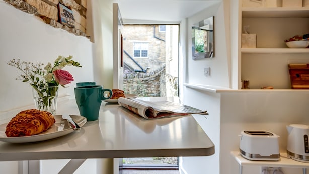 A breakfast table with a croissant, a book, and a vase of flowers.