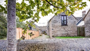 A stone building with a window and a door, surrounded by a stone wall and a wooden fence.