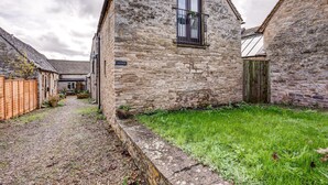 A stone building with a window and a door, surrounded by a gravel path and a grassy area.