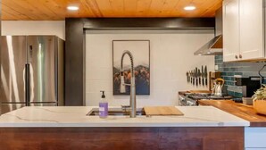A modern kitchen with stainless steel appliances, a wooden ceiling, and a white backsplash.