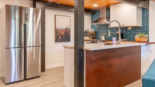 A modern kitchen with stainless steel appliances, a wooden ceiling, and a blue backsplash.