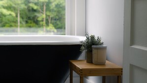 Ein Badezimmer mit einer schwarzen Badewanne, einem Holztischchen mit einem Topfpflanzen und einer weißen Tür.