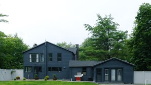 Ein Swimmingpool mit aufblasbaren Schwimmringen, ein Haus mit dunkler Fassade und zwei gestreifte Liegestühle.