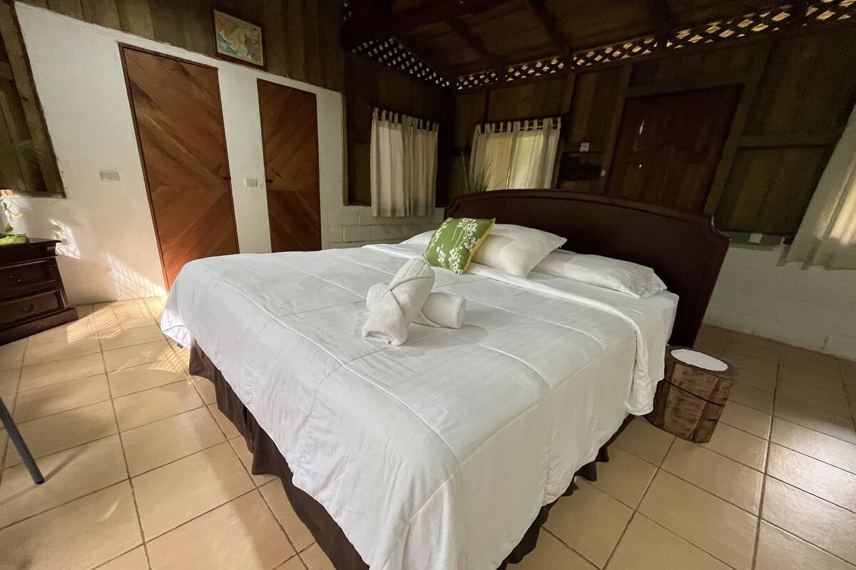 A neatly made bed with white linens and a towel, a wooden headboard, and a small bedside table with a lamp.