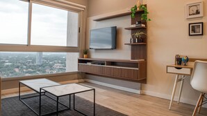 Una sala de estar moderna con un ventanal grande, un televisor de pantalla plana montado en un estante de madera, una mesita y una silla.