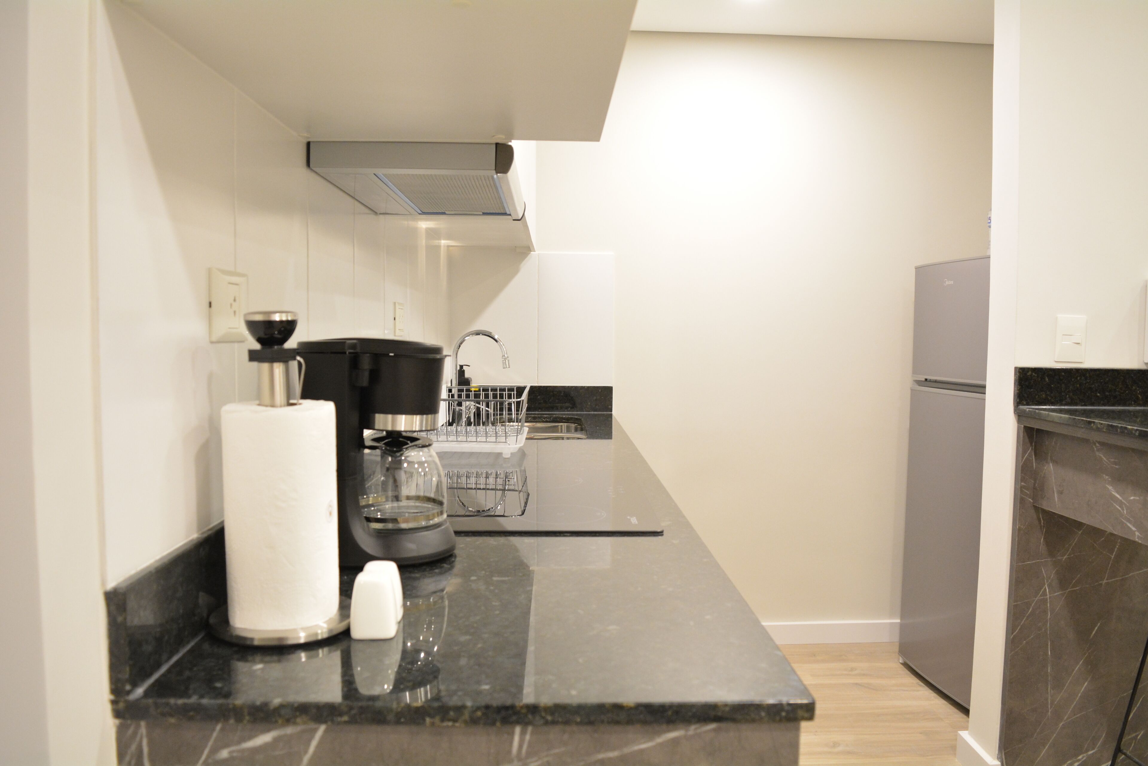 A modern kitchen with a black countertop, a coffee maker, a kettle, and a dish rack.