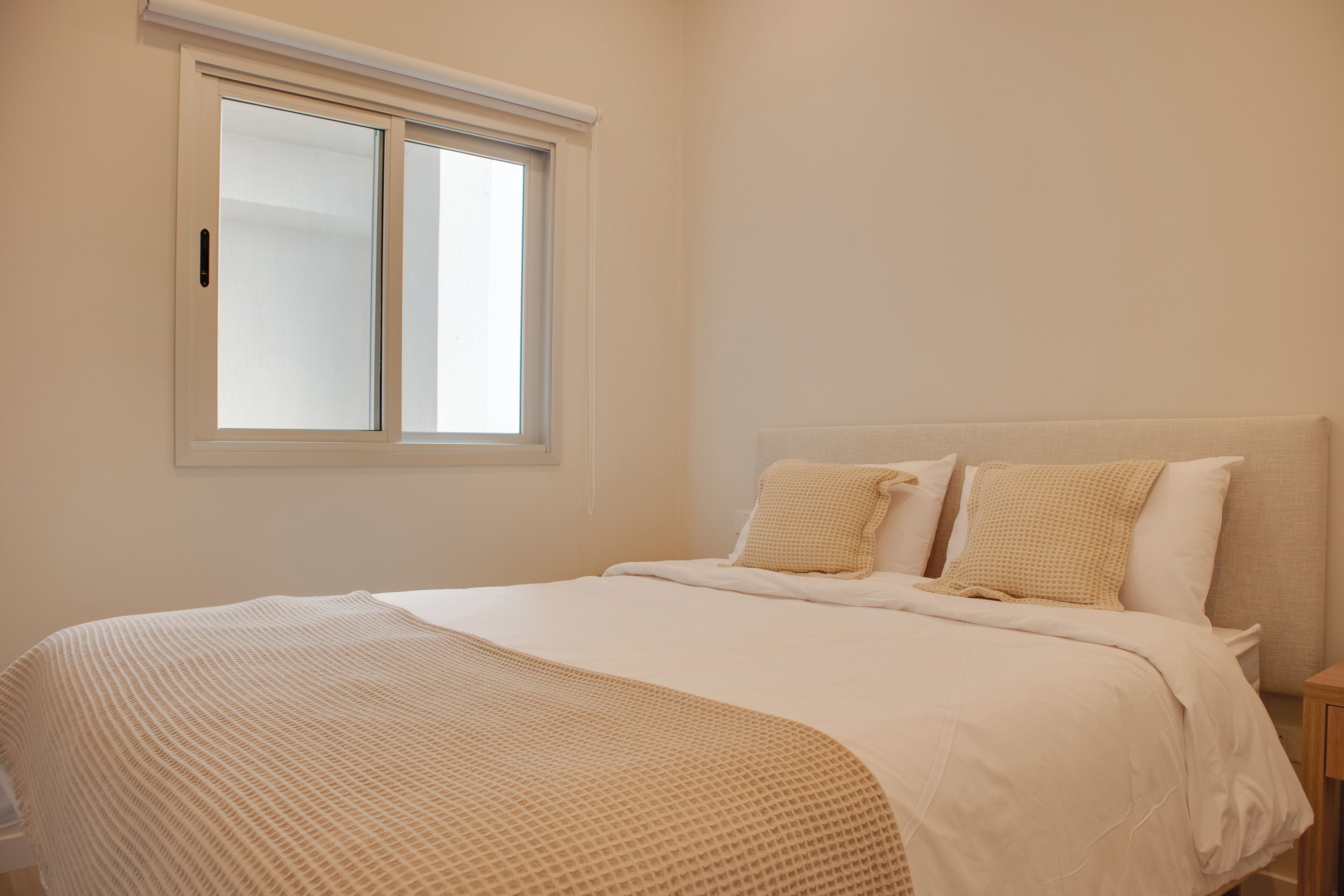 A bedroom with a large bed, two pillows, a window, and a nightstand.