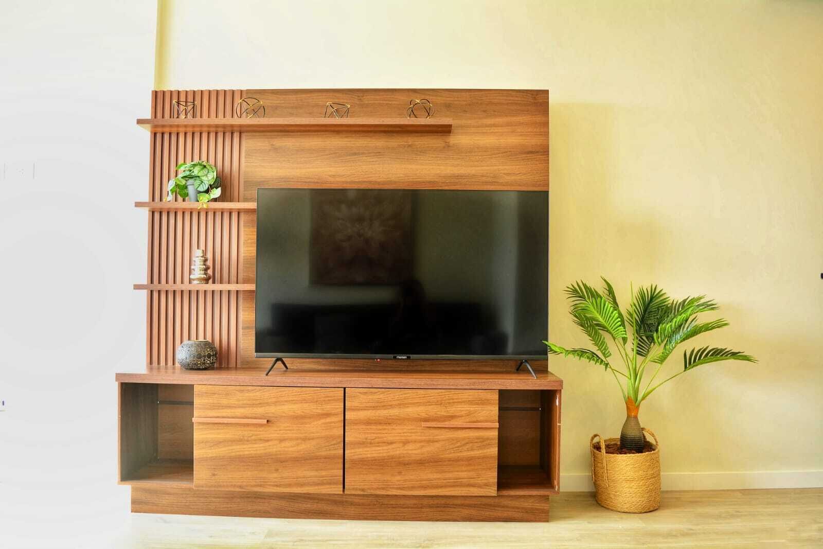 A wooden entertainment center with a flat-screen TV, shelves, and a potted plant.