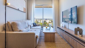 Una sala de estar moderna con un sofá, una mesa de centro, un televisor y vistas de la ciudad a través de grandes ventanales.