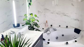 Un baño con lavamanos de mármol blanco, una bañera grande y una planta en maceta.