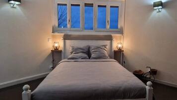 A bedroom with a bed, two bedside lamps, a window with blinds, and a wall-mounted light fixture.