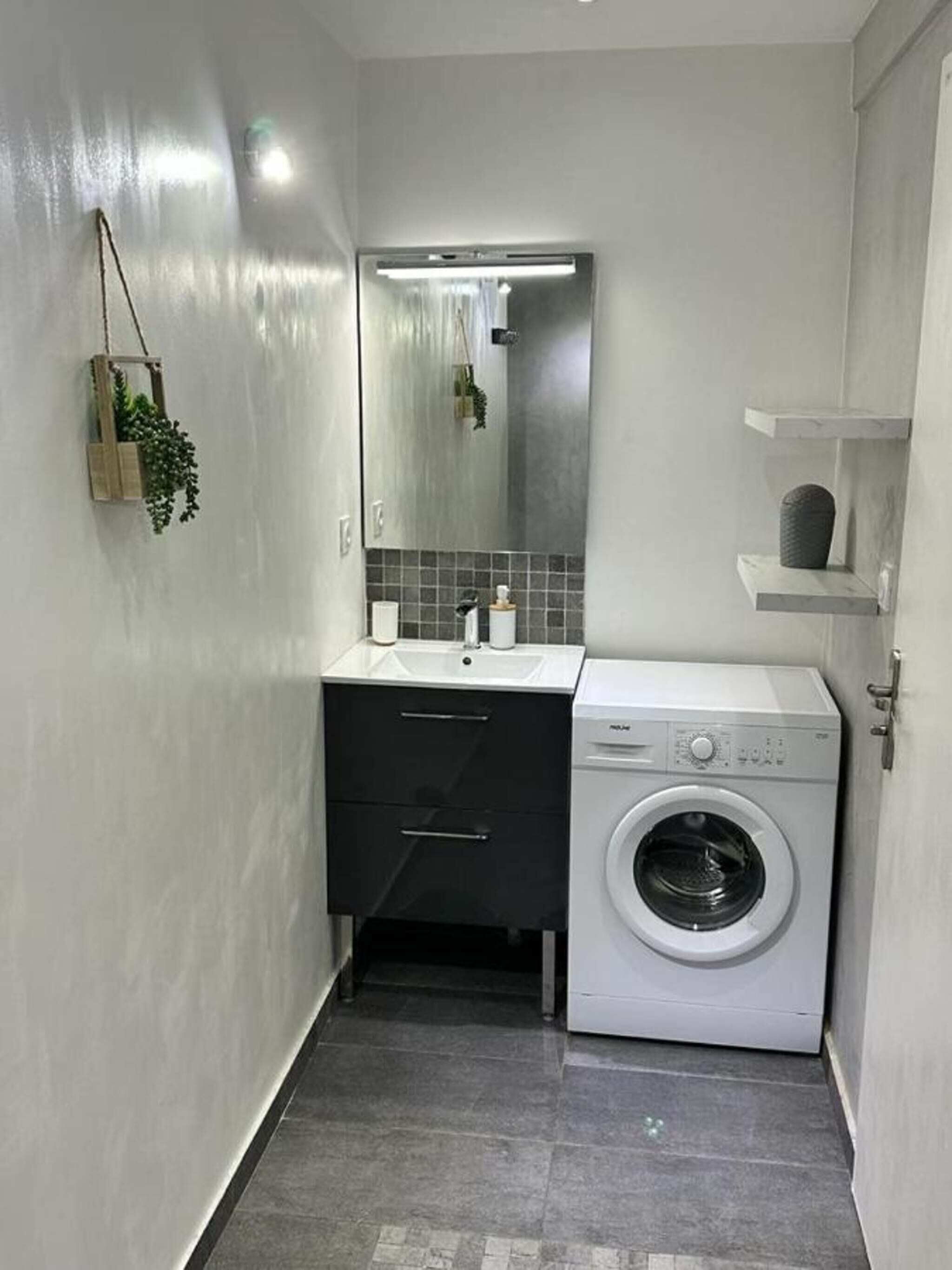 Un baño pequeño con lavadora integrada, un lavabo y un espejo.