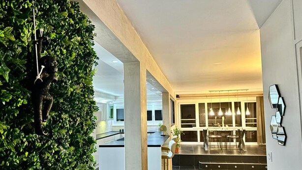 A modern kitchen with dark tiles, a bar area with stools, and a dining table with pendant lights. - L' Elegant (Douvaine)