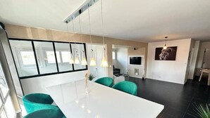 A modern kitchen with a white island, teal chairs, pendant lights, and a large window. - L' Elegant (Douvaine)
