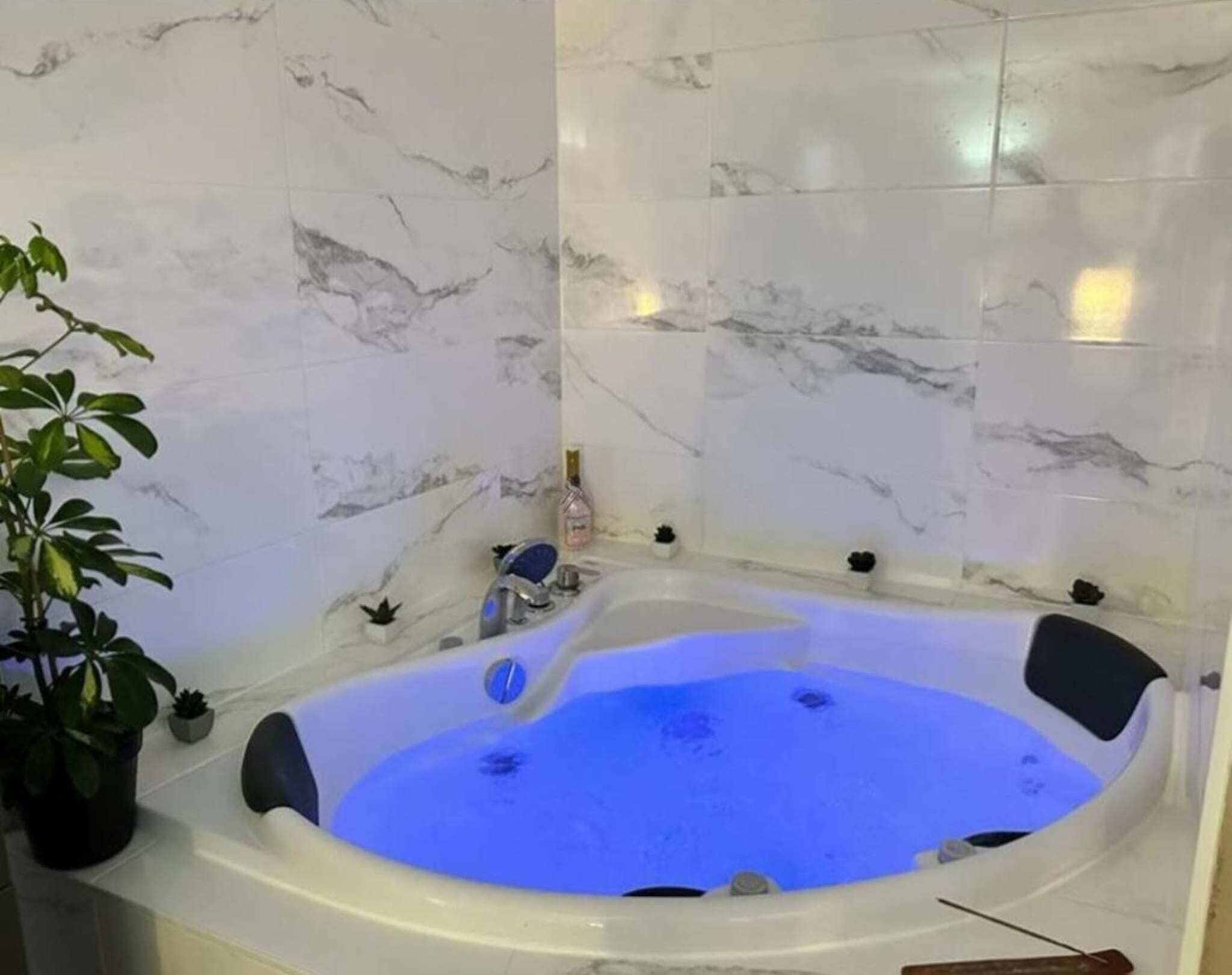 Een badkamer met een marmeren wand, een bad met blauwe verlichting en een potplant.